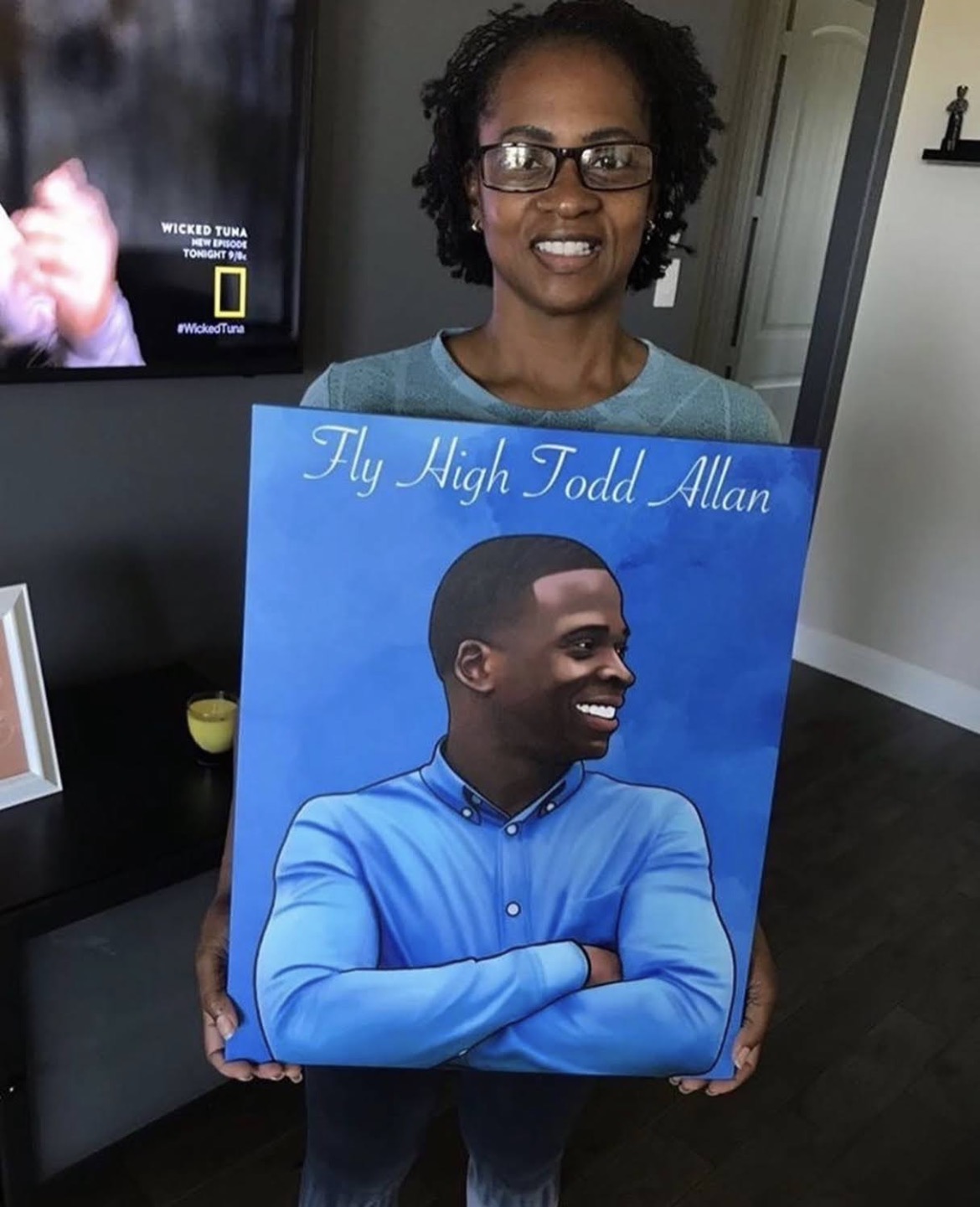 Woman holding a blue memorial portrait reading Fly High Todd Allan